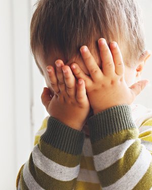 Kleinkind hält sich beide Hände vor das Gesicht.